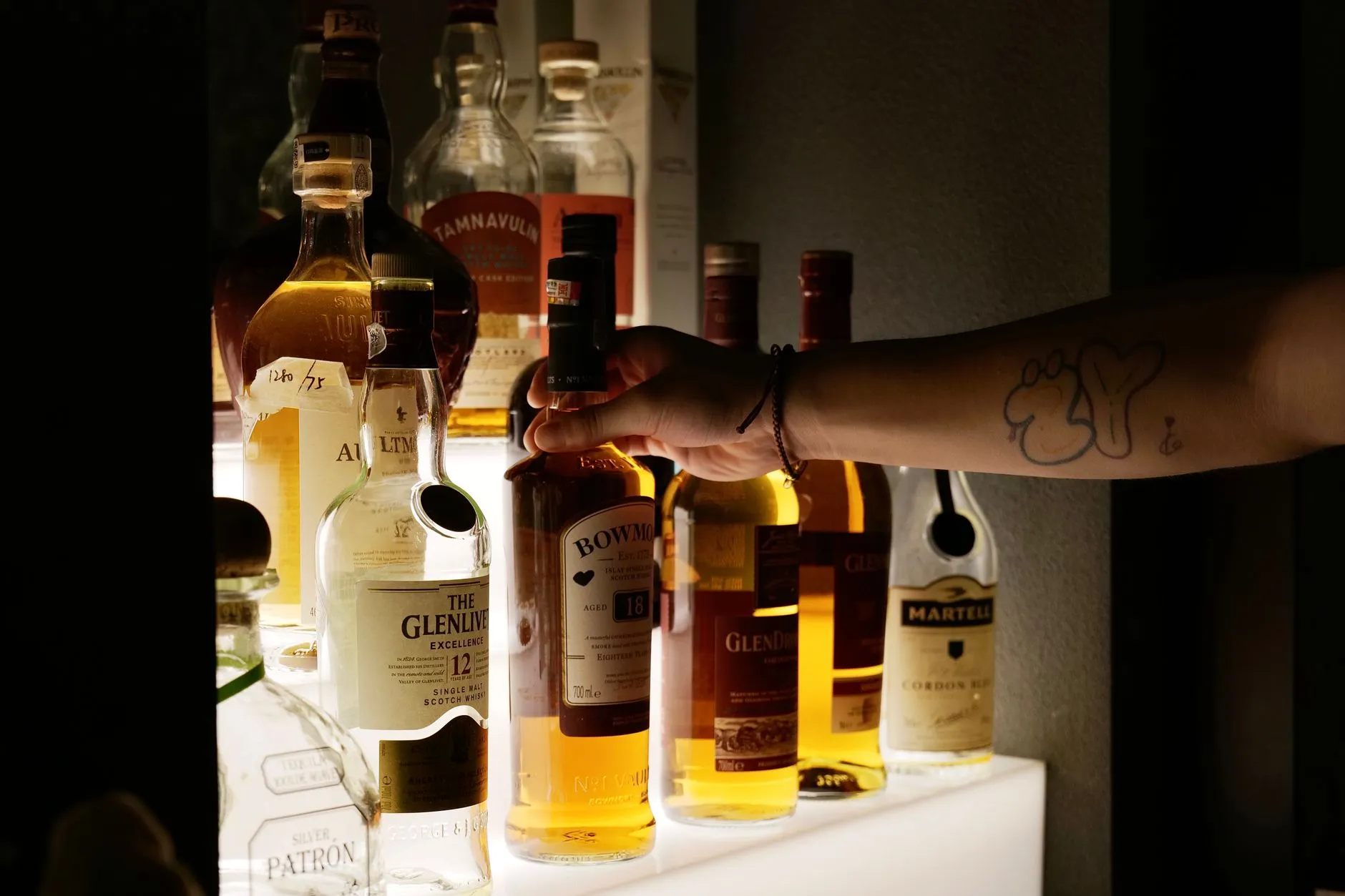 Eine Hand greift eine Whiskyflasche aus einem beleuchteten Regal