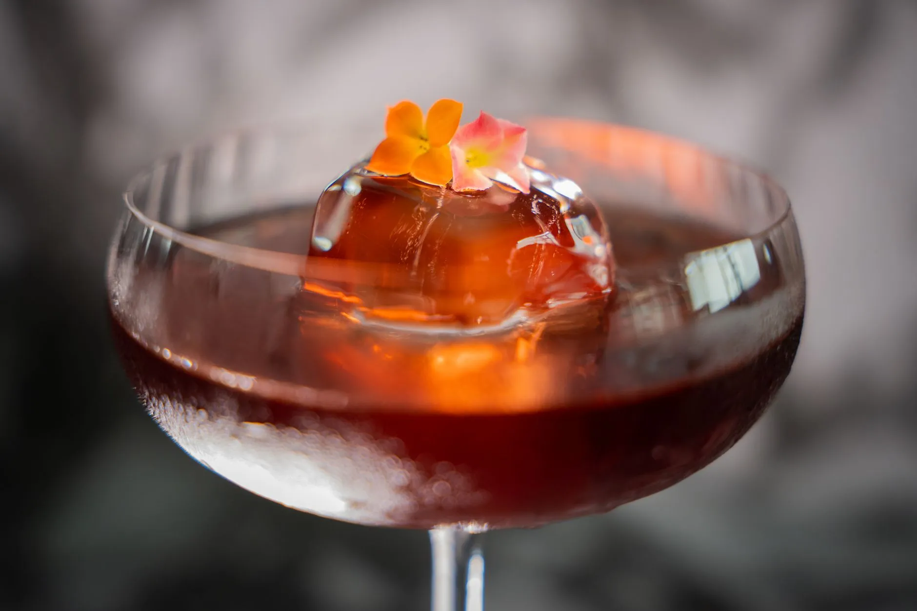Ein Cocktail mit Blüten-Garnitur und Eiskugel im Coupe-Glas