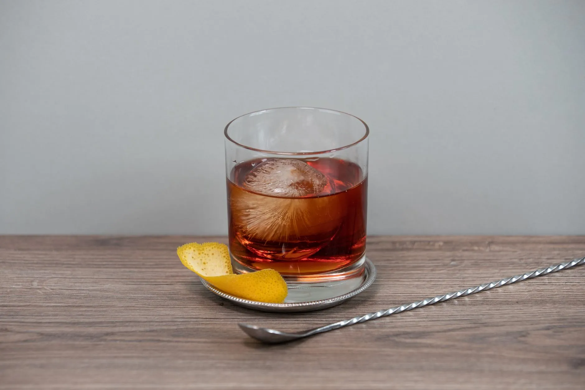 Ein Whiskycocktail mit Eiskugel und Zitruszeste