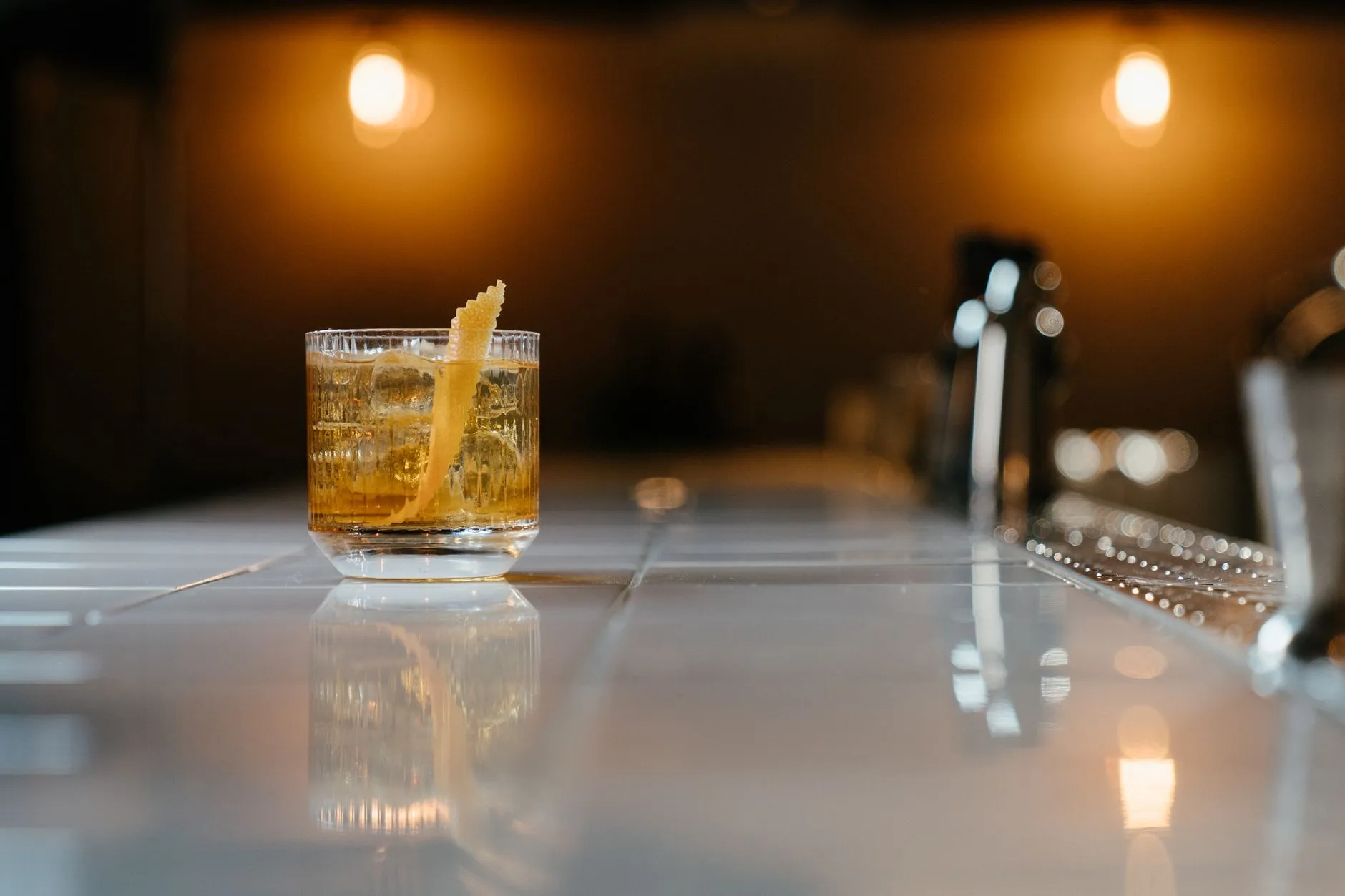 Ein Whiskycocktail mit Zesten-Garnitur auf einem Bartresen