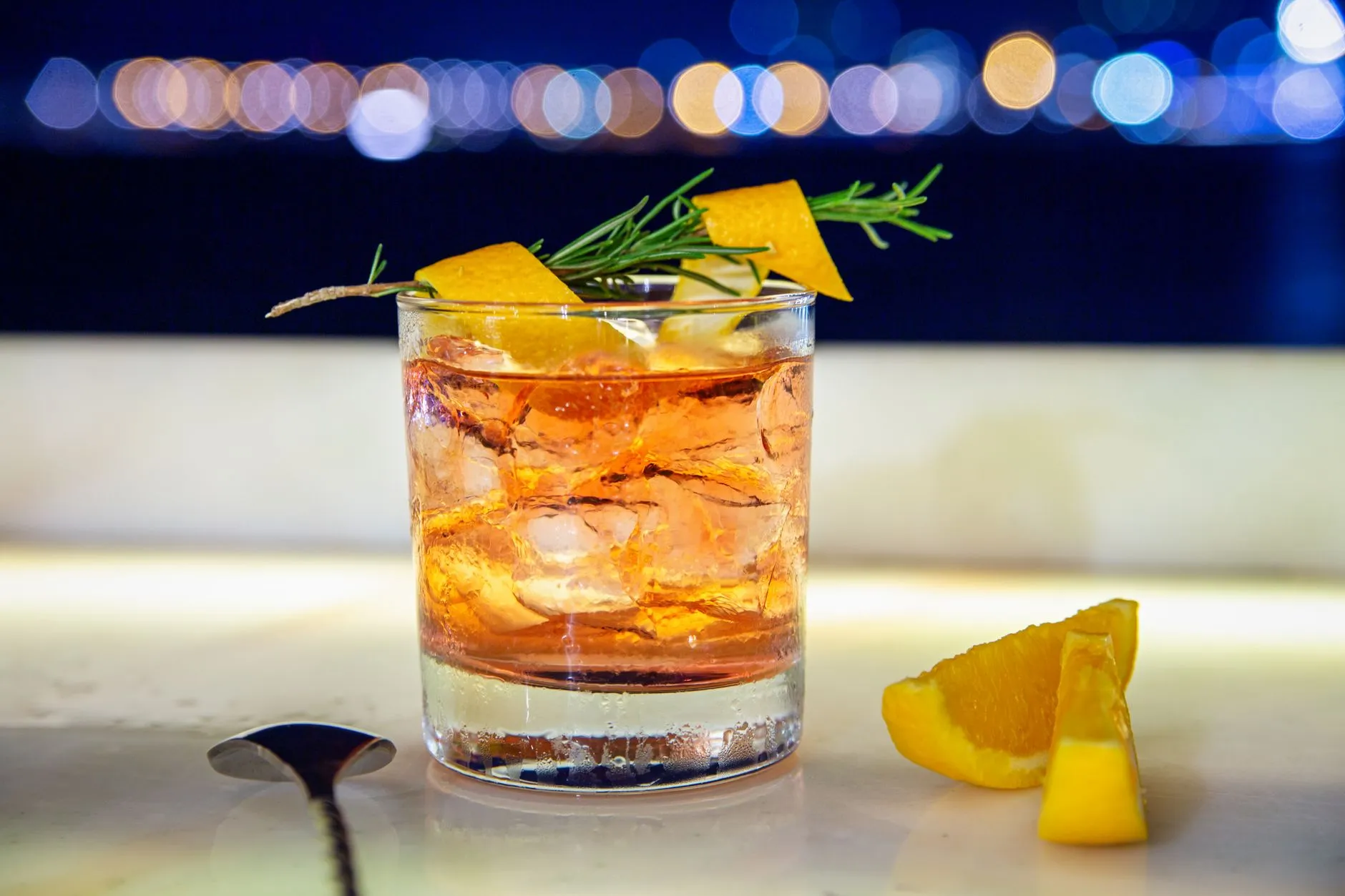 Ein Whiskycocktail mit Rosmarin und Zitrus vor dunklem Hintergrund