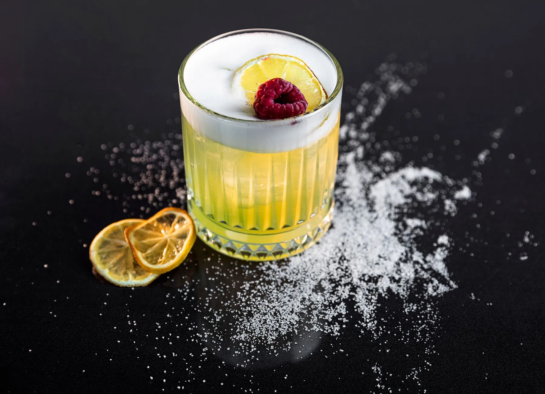 Ein Sour-Cocktail mit Zitrone im Glas vor dunklem Hintergrund